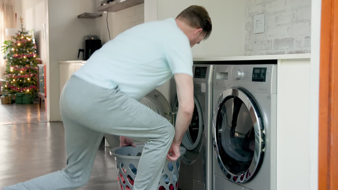 Senior man doing laundry at home, loading clothes into washing machine