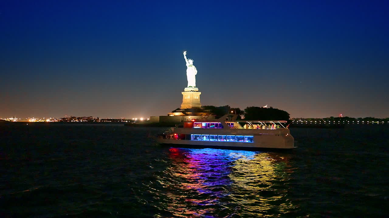 New York, USA, 8 October 2025: Boat with colorful illumination travels by the river at night. Statue of Liberty lit brightly at backdrop. River cruise in New York