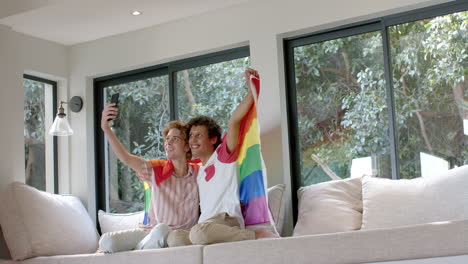 diverse gay male couple with rainbow lgbt flag, using smartphone at home, slow motion, copy space