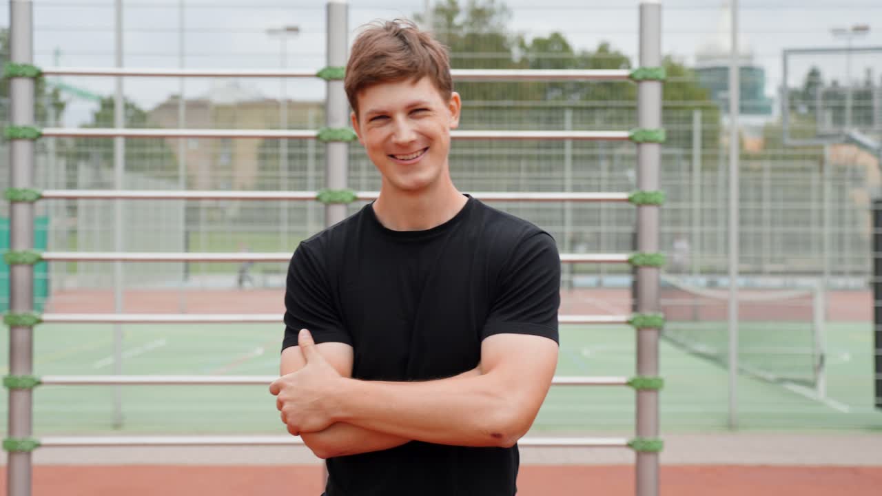 Fixed shot of young man in sportswear smiling confidently on outdoor training ground