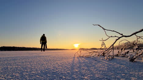 Excursionista-De-Invierno-Masculino-Solitario-Con-Mochila-Camina-A-Través-Del-Lago-Congelado-Hacia-La-Puesta-De-Sol-Dorada