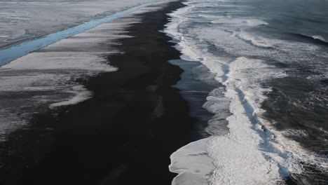 slow drone flyover black beach with foamy waves at sunset