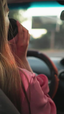 mujer conduciendo con una mano en el volante mientras bebe café con la otra, el fondo borroso muestra una carretera adelante con coches y semáforos en la distancia durante la noche