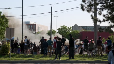 protesters watch as a car burns in the background