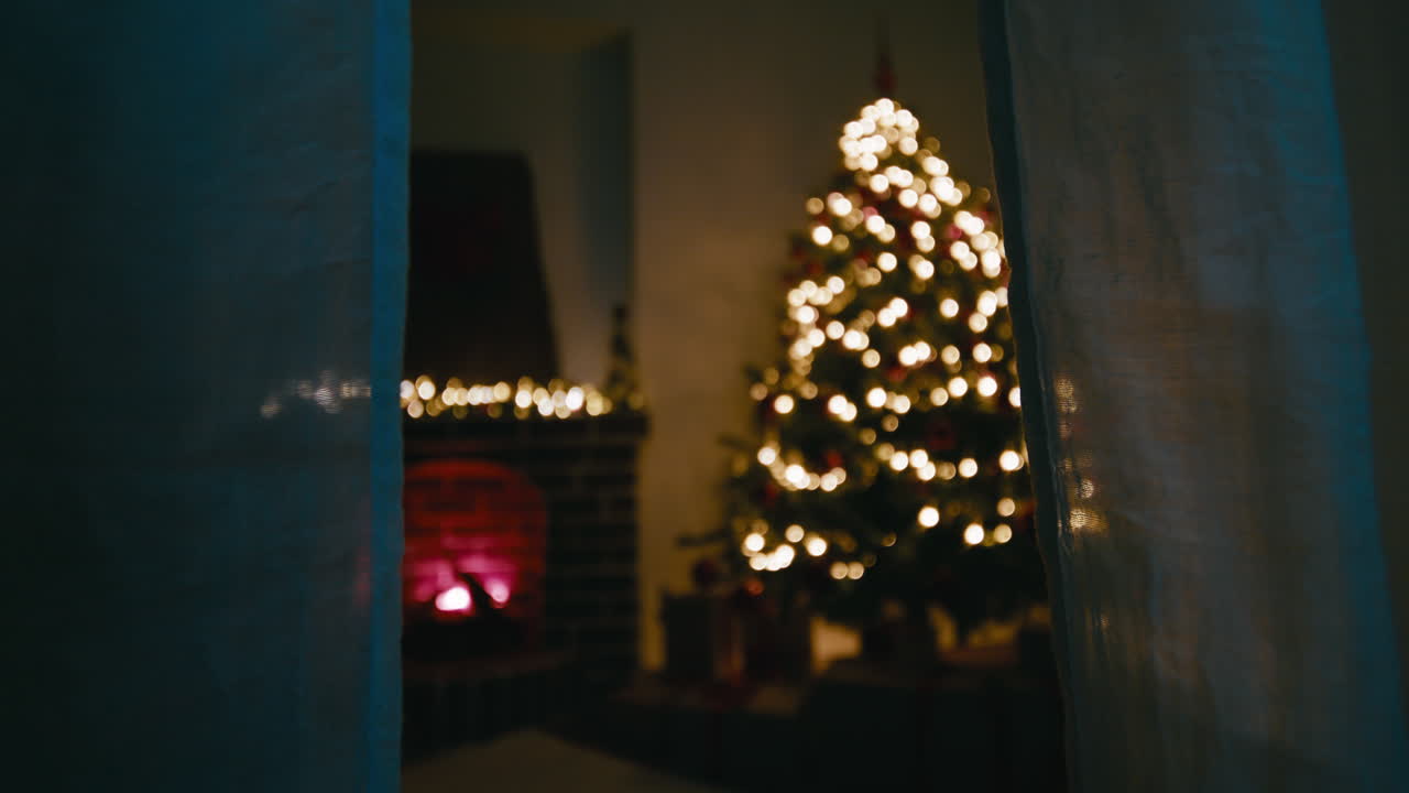 Behind the curtains of a window a bright Christmas tree in night room