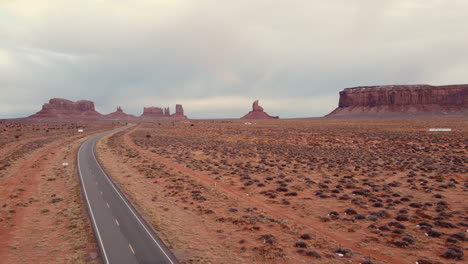 A-drone-shot-of-a-beautiful-Arizona-desert-scene-over-the-red-desert-soil,-rock-formations,-and-a-highway-disappearing-into-the-distance