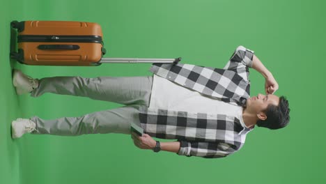 full body of asian male traveler with luggage and passport smiling and flexing his bicep while standing in the green screen background studio