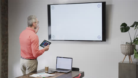 un hombre de negocios caucásico haciendo una llamada de video usando una tableta y un monitor con espacio de copia, cámara lenta
