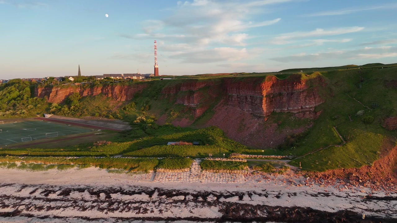 Ripresa aerea di un altopiano con scogliera sulla spiaggia e un campo sportivo vicino alla costa settentrionale di Helgoland.