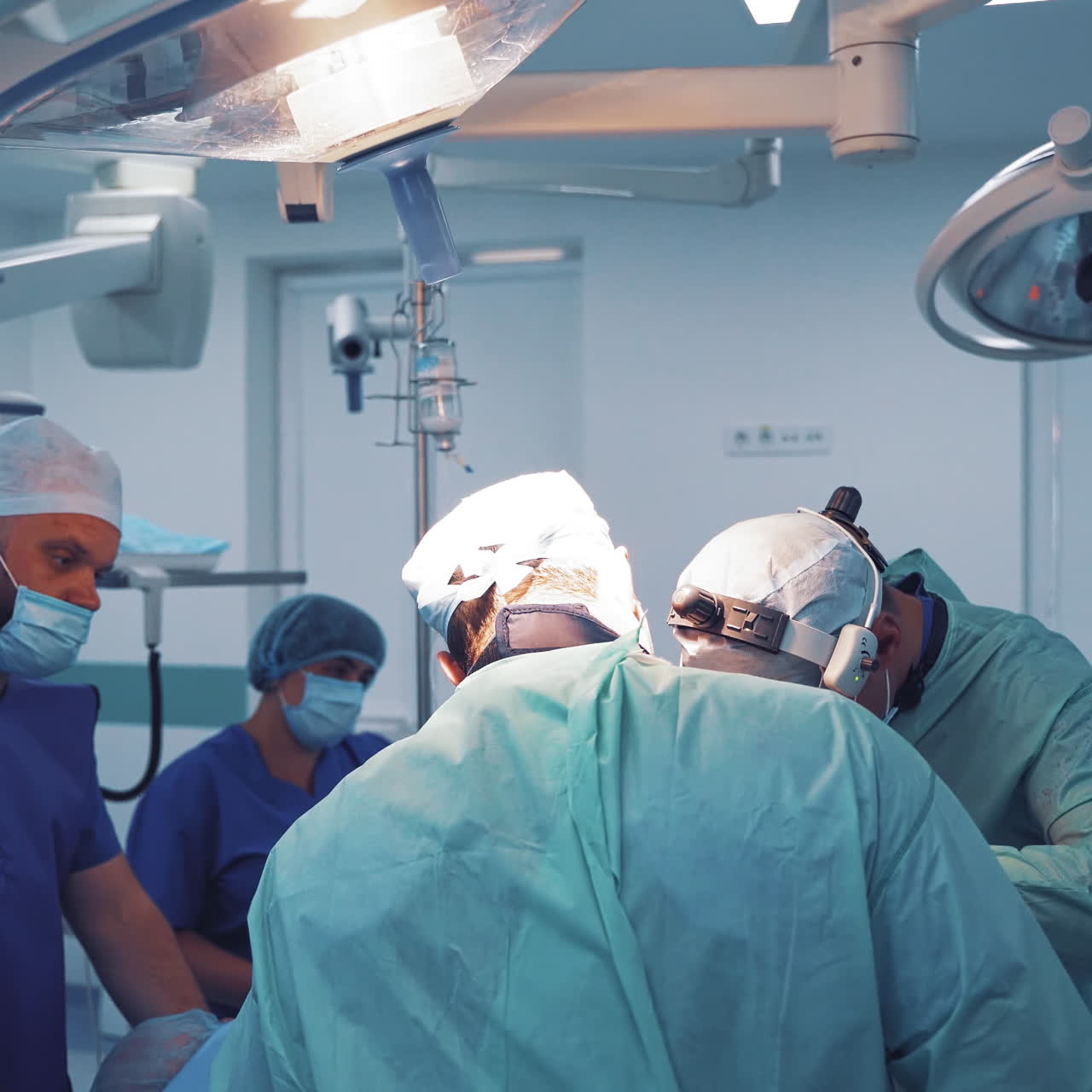 Group of doctors in medical clothing perform an operation in clinic. Medical background of operating room with specialists working during the operation among modern equipment.