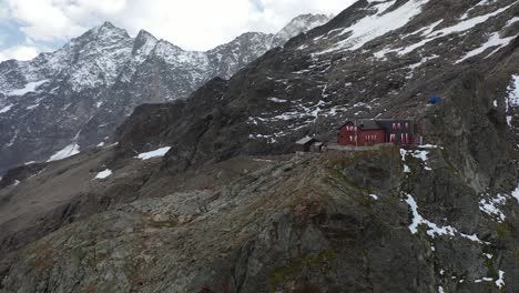 Circling-drone-shot-of-the-Dossen-Hut-on-the-peak-of-the-mountain-in-Switzerland-during-a-beautiful-and-dramatic-summer-day-with-snow-covered-mountains-in-the-background