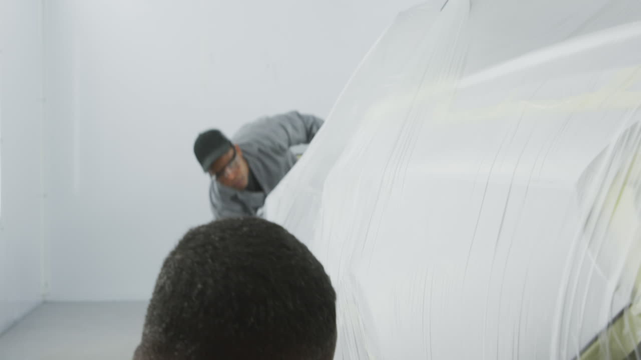 Two African American male car mechanic putting a protective cover on a car 