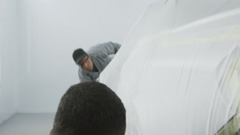 two african american male car mechanic putting a protective cover on a car