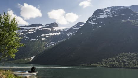 boat moored on the lakeside at the fjord during winter with rocky mountain in the background - motion time lapse