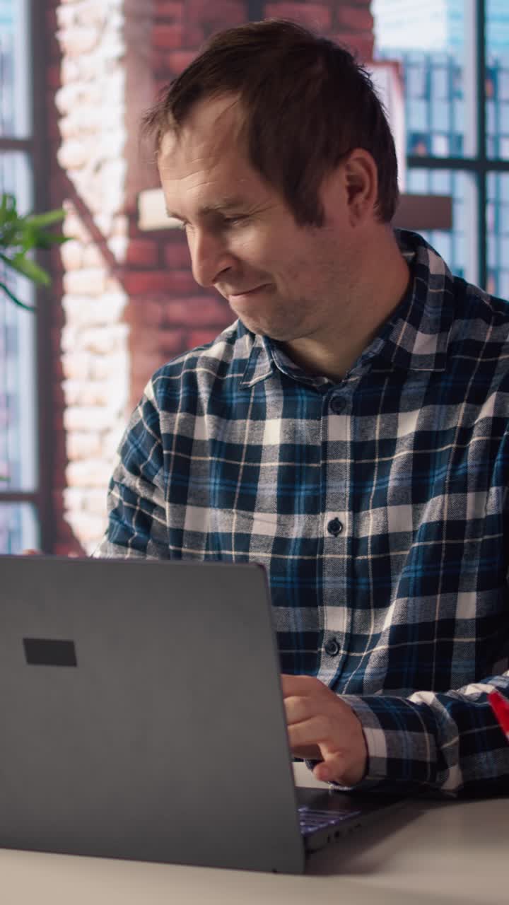 Vertical video Freelancer in home office sitting at desk in front of laptop, answering phone call