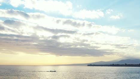 fishing boat sailing across calm sea reflecting glowing sky with grey clouds hiding sun setting down the horizon in cambodia