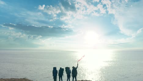 바다 근처의 모래 바위 꼭대기에 서 있는 불 지이를 가진 여행자 들
