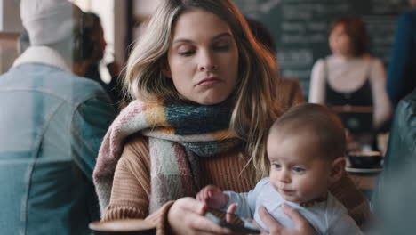 junge mutter mit baby im café mit smartphone, trinkt kaffee, entspannt sich in einem belebten restaurant und genießt die mutterschaft