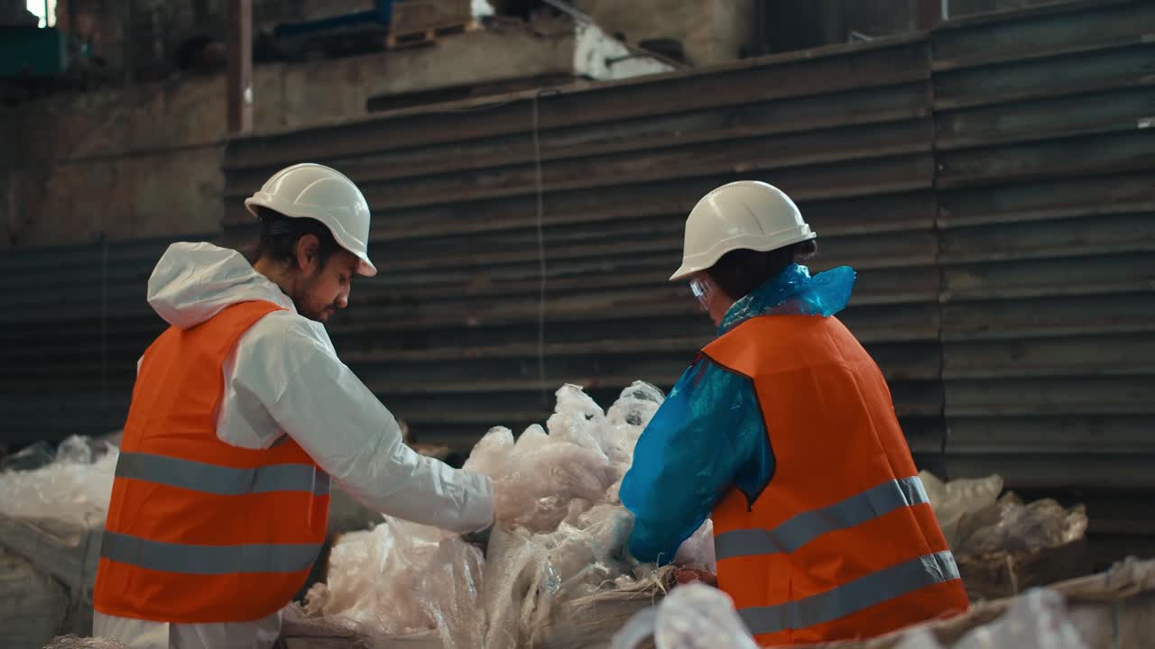 un hombre moreno con barba en un uniforme de protección blanco y un chaleco naranja junto con una chica morena presiona celofán plástico mientras trabaja en una planta de procesamiento y clasificación de residuos
