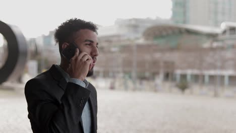 smiling young man having conversation through modern phone outdoor