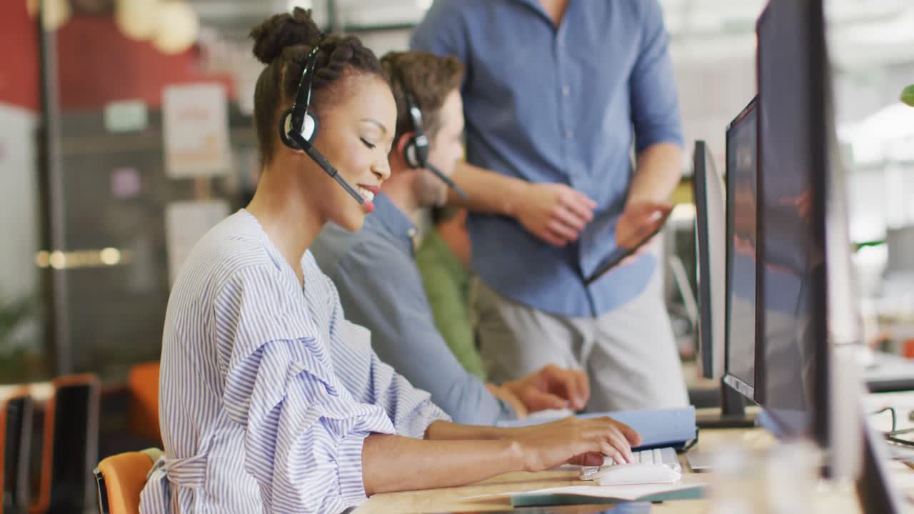 Happy diverse business people sitting at table and using phone headsets at office