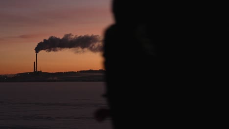 person walks in front of the camera, silhouette of smoking power plant on the background