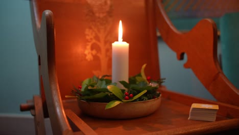 Static-close-up-shot-of-Christmas-candle-with-holly-leaves-around,-placed-on-wooden-chair