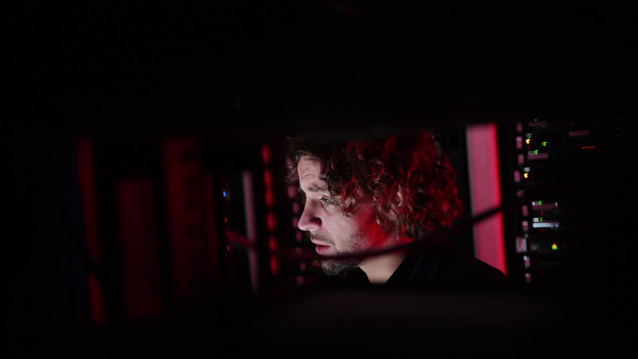 A man and a woman trying to fix an error in a server room with flashing red lights
