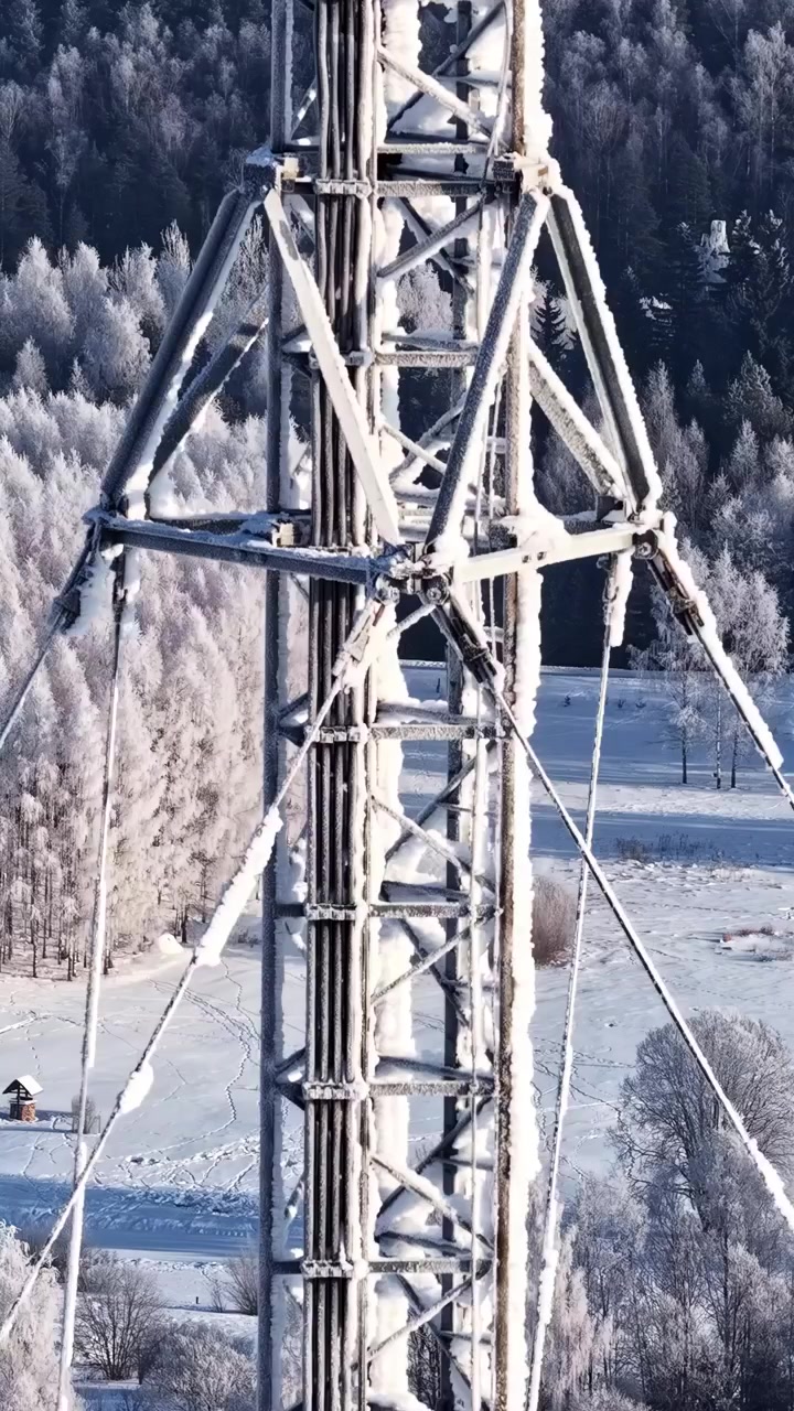 Ein vereister Kommunikationsturm steht in einer verschneiten ländlichen Landschaft inmitten von bereiften Bäumen.