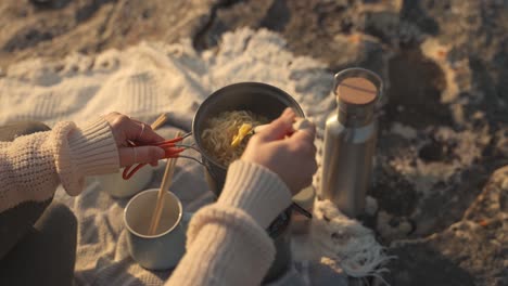 Slow-motion-footage-of-a-woman-cooking-noodles-in-a-small-pot-outdoors-at-sunset