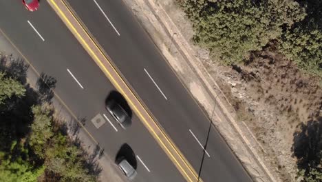 Cars-driving-on-two-lane-asphalt-road-through-nature,-aerial-top-down-view