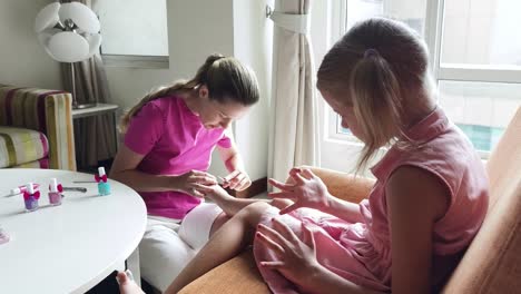 mother doing nail art for her daughter at home