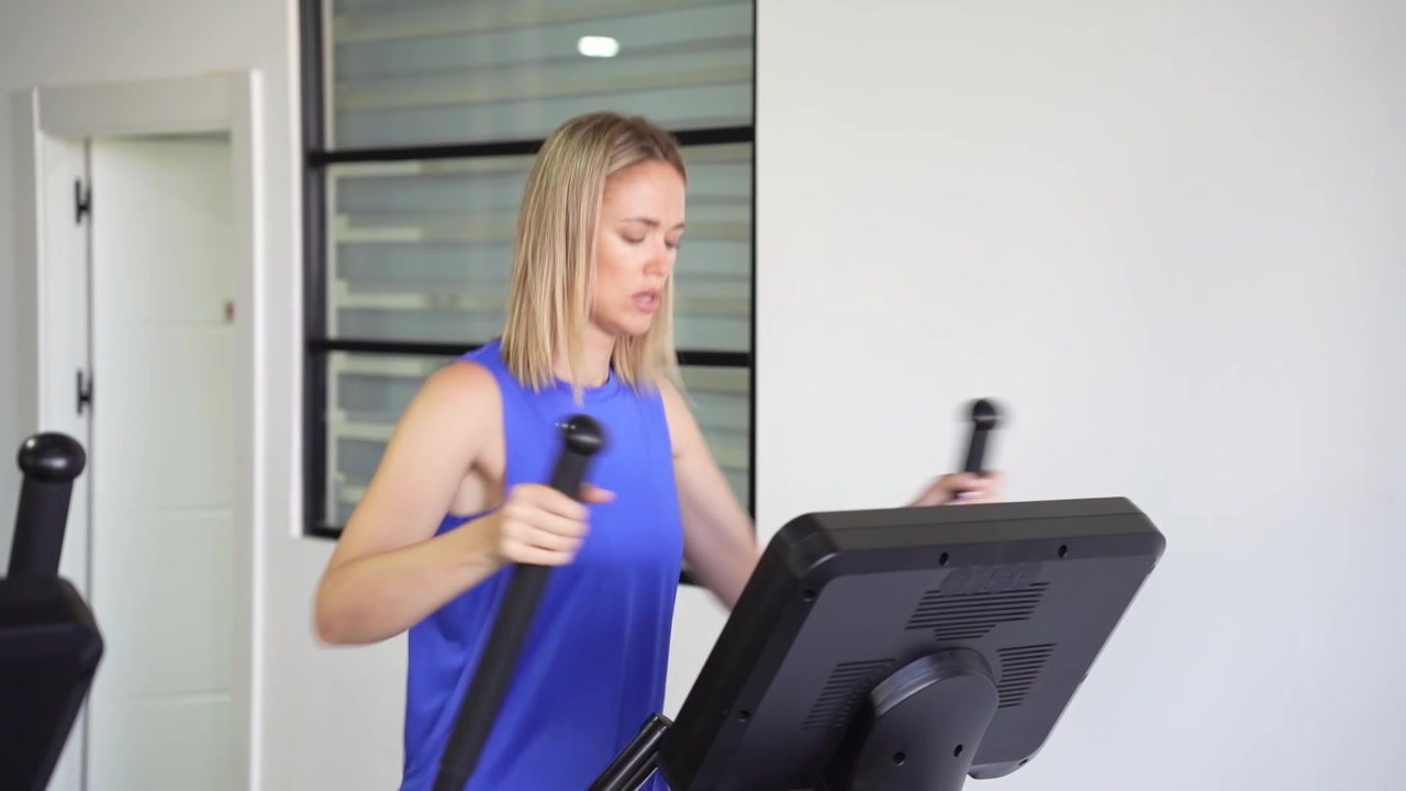Una donna si allena su un'ellittica in una palestra moderna, concentrata sulla sua salute e forma fisica.