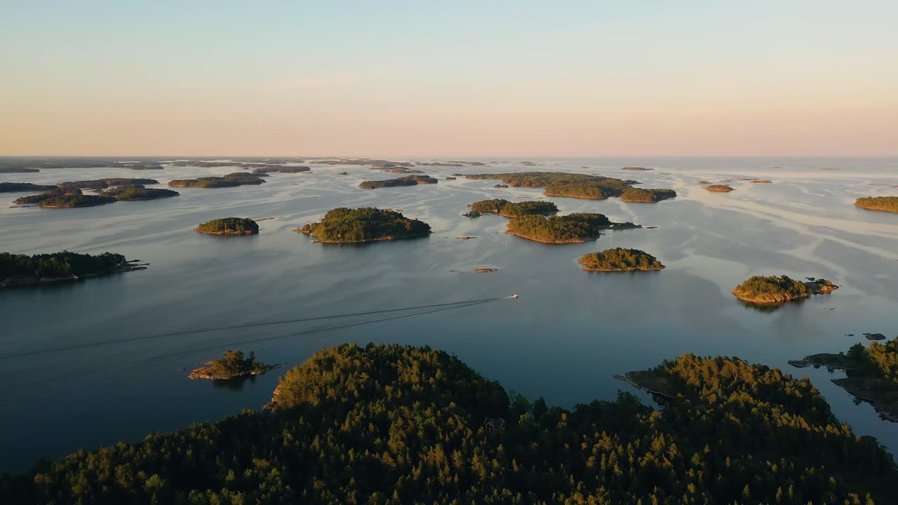 Aerial view of a boat, driving in middle of islands, colorful, summer sunset, in the archipelago, in Scandinavia - tracking, tilt up, drone shot