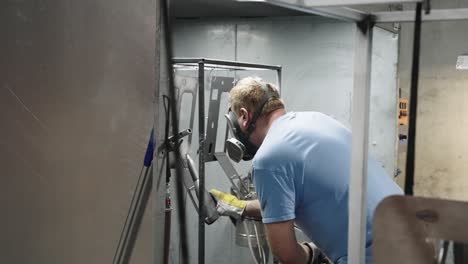 slow motion, blue collar worker applying powder coating on metal with paint gun in workshop