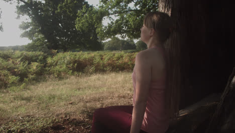 a young girl sitting and taking deep breath beneath the shadow of the tree in the park outdoor on a sunny day