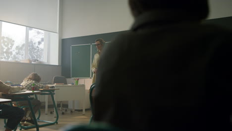 students sitting at desks in classroom. teacher explaining lesson to pupils