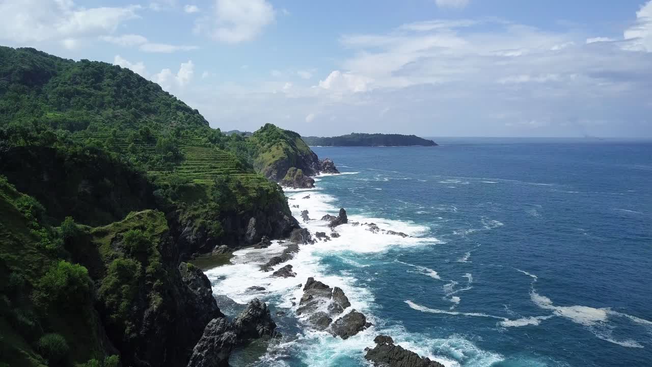 impresionantes imágenes de drones de un vuelo sobre las verdes montañas cubiertas de bosques con terrazas agrícolas que bordean el océano en indonesia