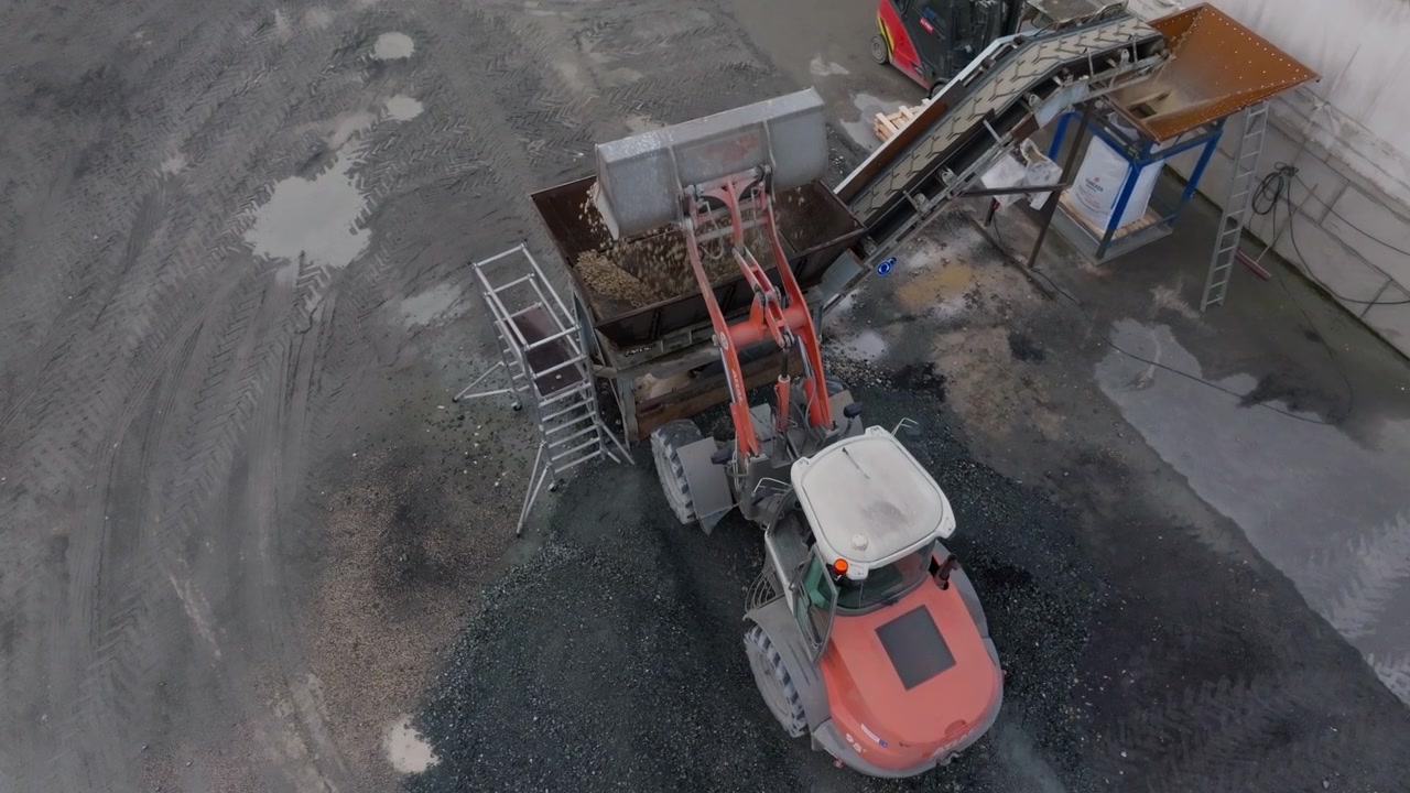 Aerial View, loader feeding aggregate into a hopper at a quarry processing plant, showing conveyor machinery, raw material handling, construction, and mining industry themes