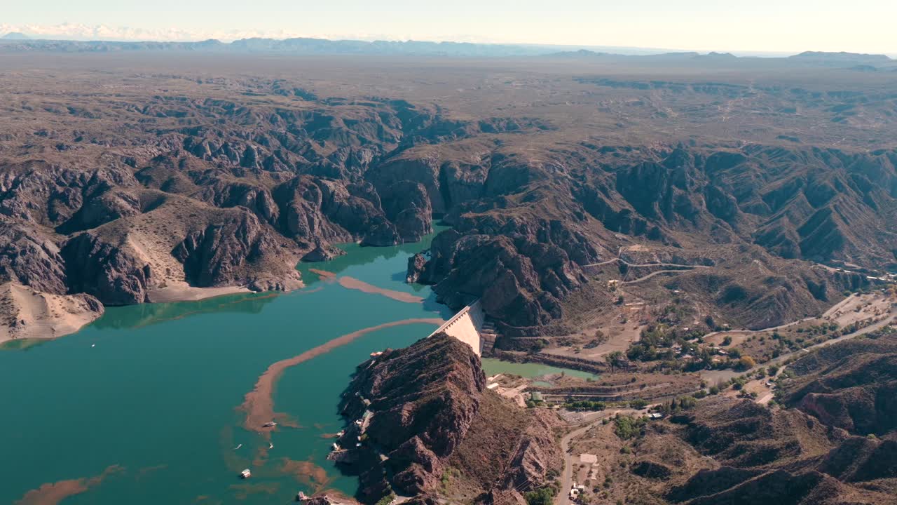 Aerial view of Atuel Canyon with dramatic rocky cliffs, a winding turquoise river, and a large dam in Mendoza, Argentina.