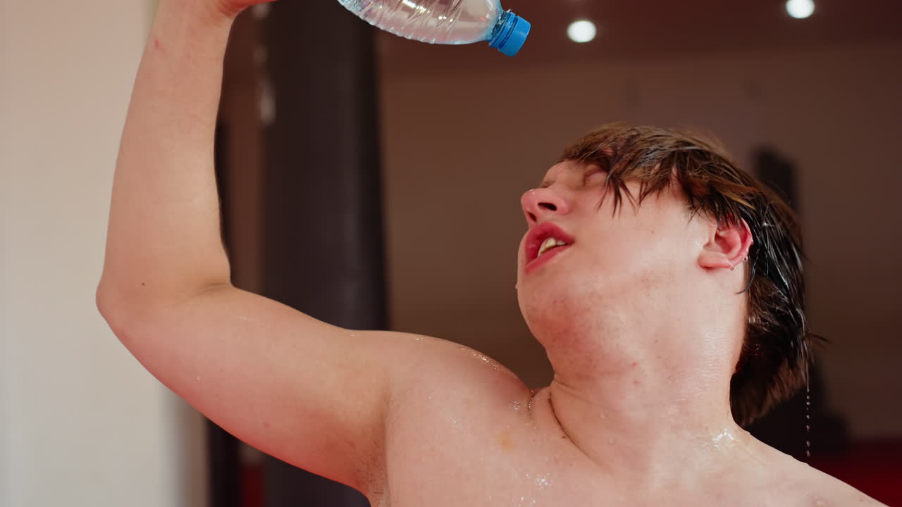 Shirtless young man cooling down after workout pouring water on chest from bottle, refreshing body with droplets running down skin, moment of relief, hydration and recovery in training environment