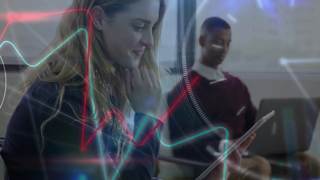 Mulher tocando e deslizando no tablet, manipulando gráficos de tecnologia e tickers de dados enquanto um colega digita no laptop.