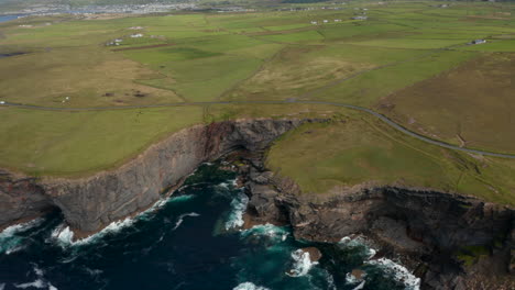 Toma-Panorámica-Aérea-De-Verdes-Praderas-A-Lo-Largo-De-La-Costa-Del-Mar.-Acantilados-Rocosos-Altos-Y-Dentados-Por-Encima-De-Las-Olas-Rompientes.-Paseo-Del-Acantilado-De-Kilkee,-Irlanda