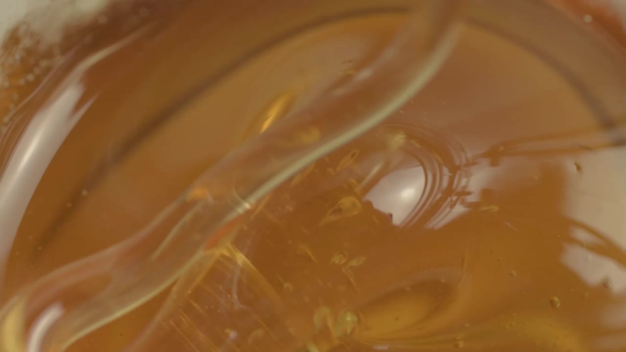 Clear golden runny honey dripping into a jar macro