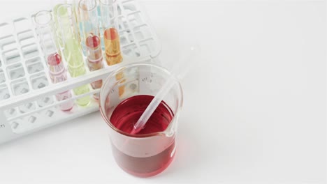 Coloured-liquid-in-flask-with-test-tubes-in-stand-on-white-background-with-copy-space,-slow-motion