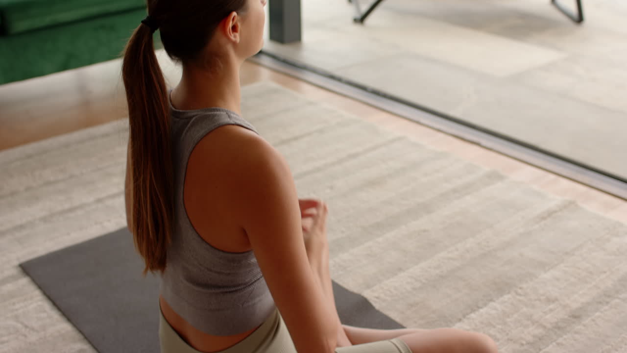Meditating on yoga mat, woman practicing mindfulness at home near window
