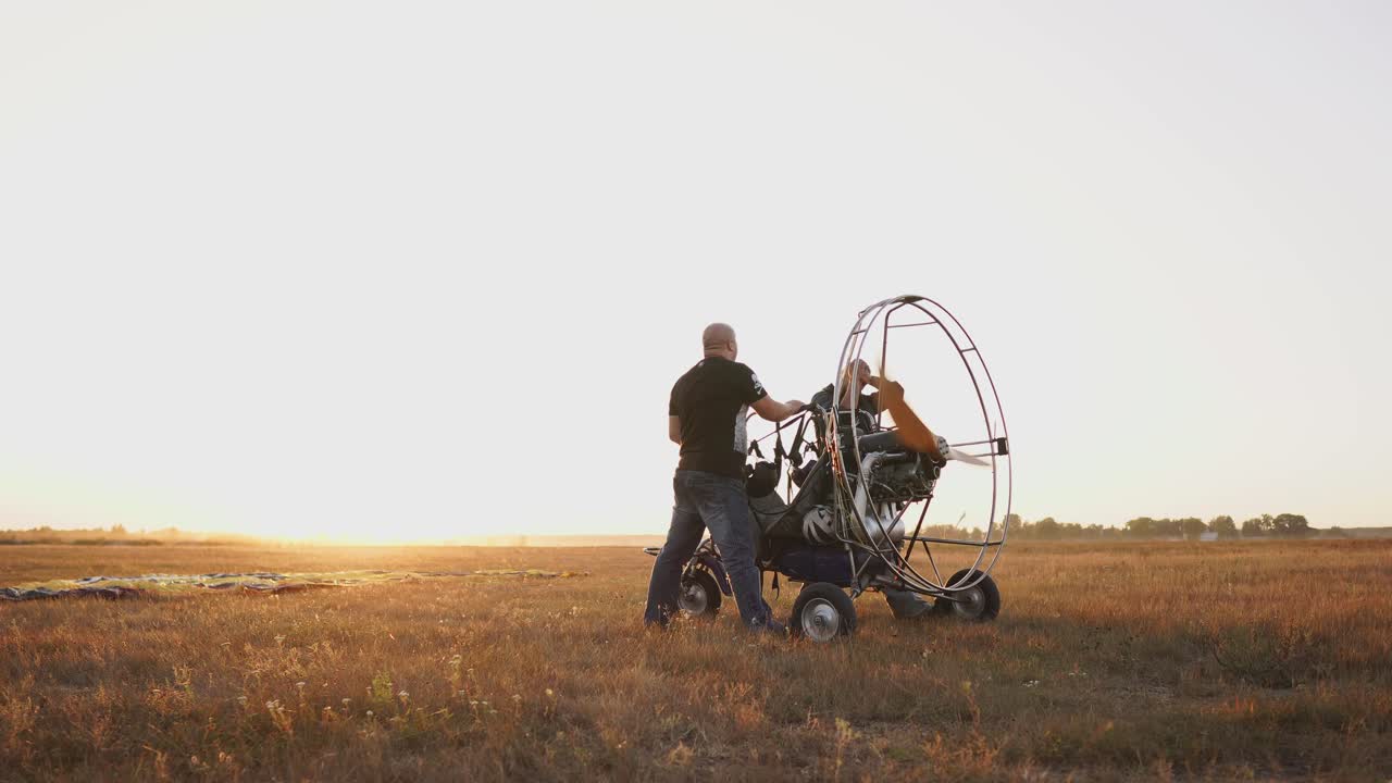 모터 패러글라이더는 해가 지는 시점에 나무 프로펠러로 필드에 서 있으며, 두 명의 조종사가 비행 전에 엔진의 테스트 런을 수행합니다.