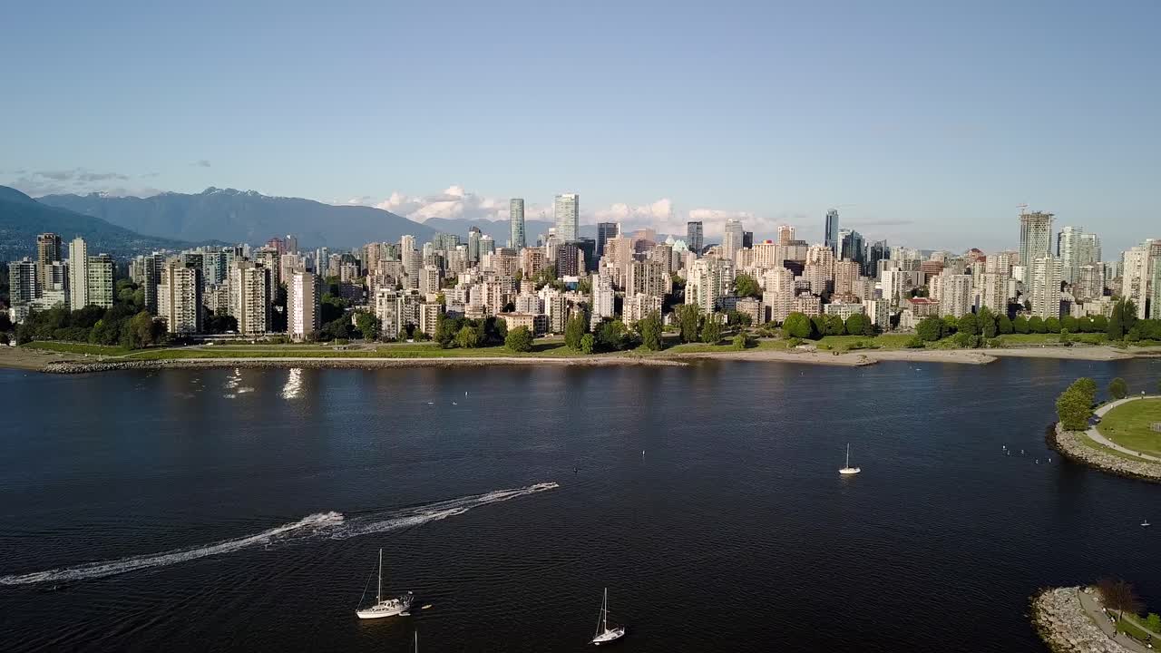 인기 있는 키트실라노 해변, 보트와 제트 스키가 있는 키트 해변은 캐나다 브리티시 컬럼비아 밴쿠버에 있는 다운타운 스카이라인과 잉글리시 베이가 있는 푸른 바다에 여파를 남기고 있습니다.