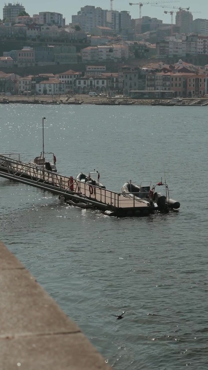 Pontile galleggiante con piccole imbarcazioni sul fiume Douro e il lungomare di Porto sullo sfondo.