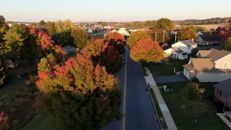 aerial dolly shot during sunset in pennsylvania autumn, colorful leaves, street, homes, community center nearby